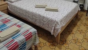 Ein Einzelbett mit blumigem Überwurf, ein Nachttisch, eine kleine Nachttischlampe, ein Fenster mit herzförmigen Vorhängen und ein gemusterter Boden.