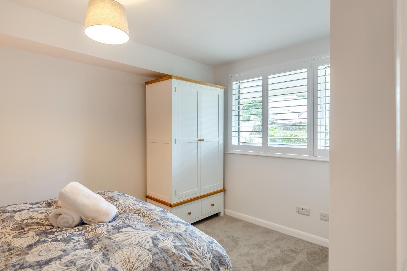 A bedroom with a bed, a wardrobe, a window with blinds, and a ceiling light.