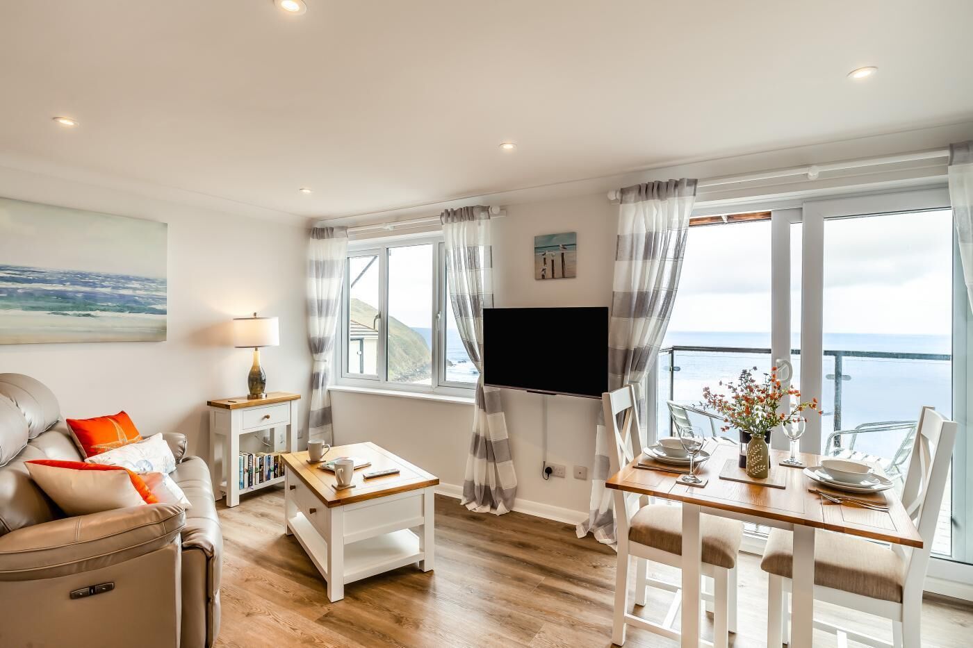 A living room with a sofa, a coffee table, a TV, and a dining area with a table set for two.
