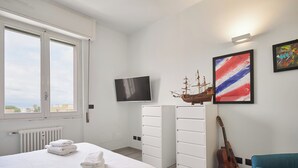 Una camera da letto con un letto, una TV, un modellino di nave, una chitarra e una sedia blu.