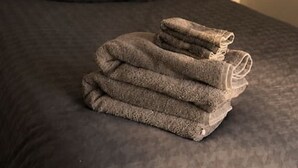 En pænt redt seng med et sammenfoldet håndklæde og en pude på en mørk madras.