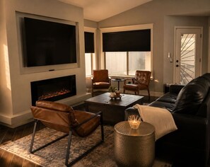 Ein Wohnzimmer mit Kamin, Ledersesseln, einer Couch, einem Couchtisch und einem an der Wand befestigten Fernseher.