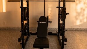 Et hjemmegymnasium med bænkpresser, squat stativ og forskellige vægtskiver.