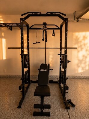 Ein Heimfitnessraum mit Langhantelbank, Kniebeugestange und verschiedenen Gewichtsplatten.