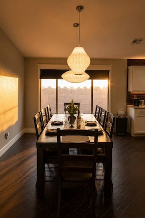 A dining area with a large table, chairs, a hanging light fixture, and a view through the windows. - Desert Disconnect | Outdoor Cinema • Pool (Mesa)