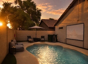 A swimming pool with lounge chairs and a projector screen, surrounded by a brick wall and trees. - Desert Disconnect | Outdoor Cinema • Pool (Mesa)