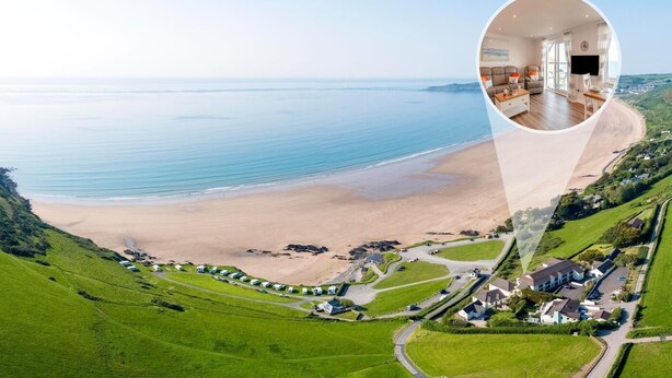 Une propriété située sur la côte, offrant une vue sur la plage, un grand espace de vie avec une grande fenêtre et une pelouse bien entretenue.