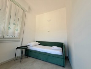 A small, single-bed room with a green headboard, a small round table, and a window with a white curtain. - Peonie 5 - Two Bedroom Apartment, Sleeps 5 (Rapallo)