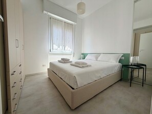 Une chambre à coucher comprenant un lit, une commode, une fenêtre avec des rideaux, une table de chevet avec une lampe et un mur d’accent de couleur verte.