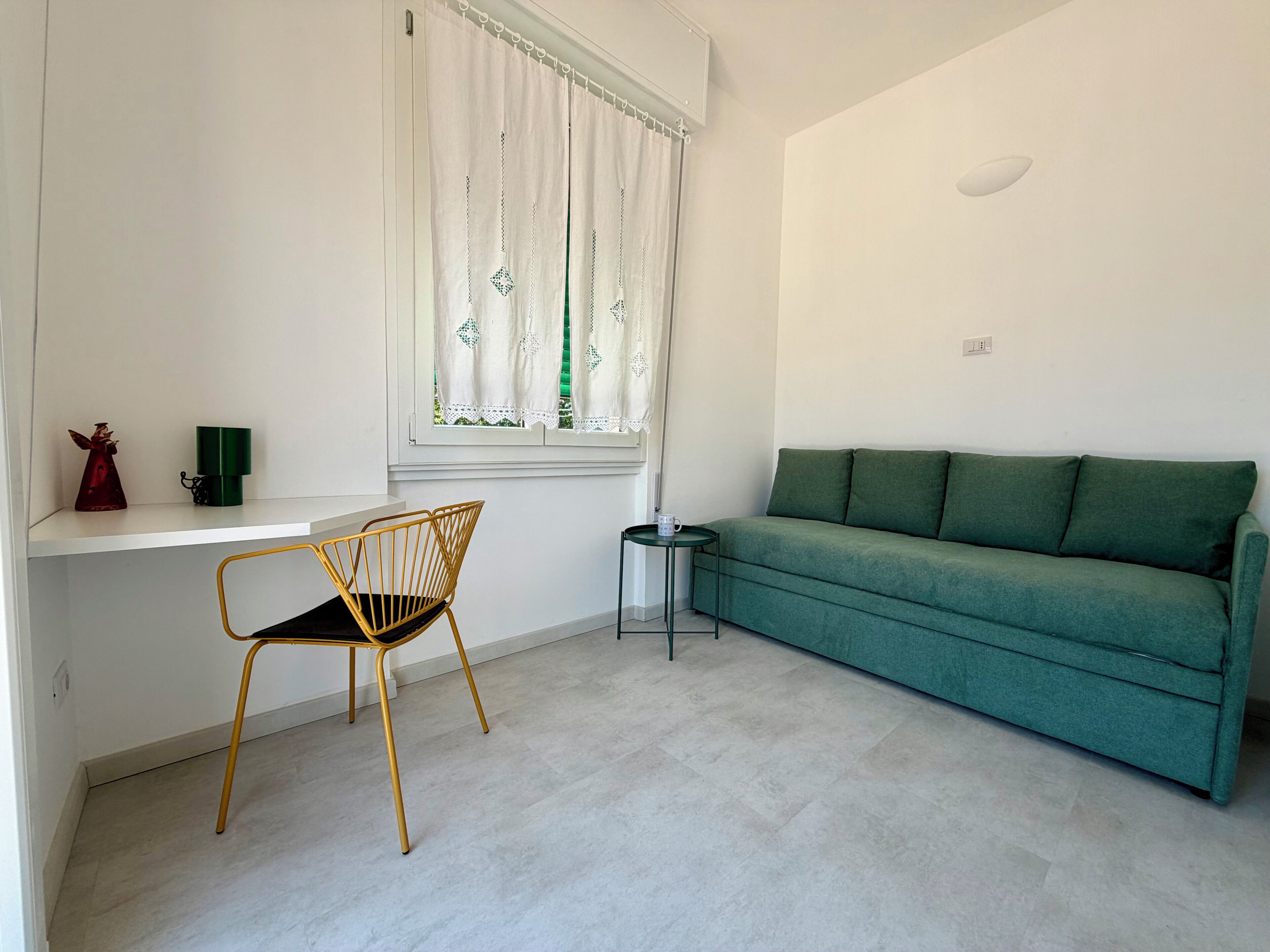 Una habitación con un sofá verde, una silla amarilla, una mesita y una ventana con cortinas.