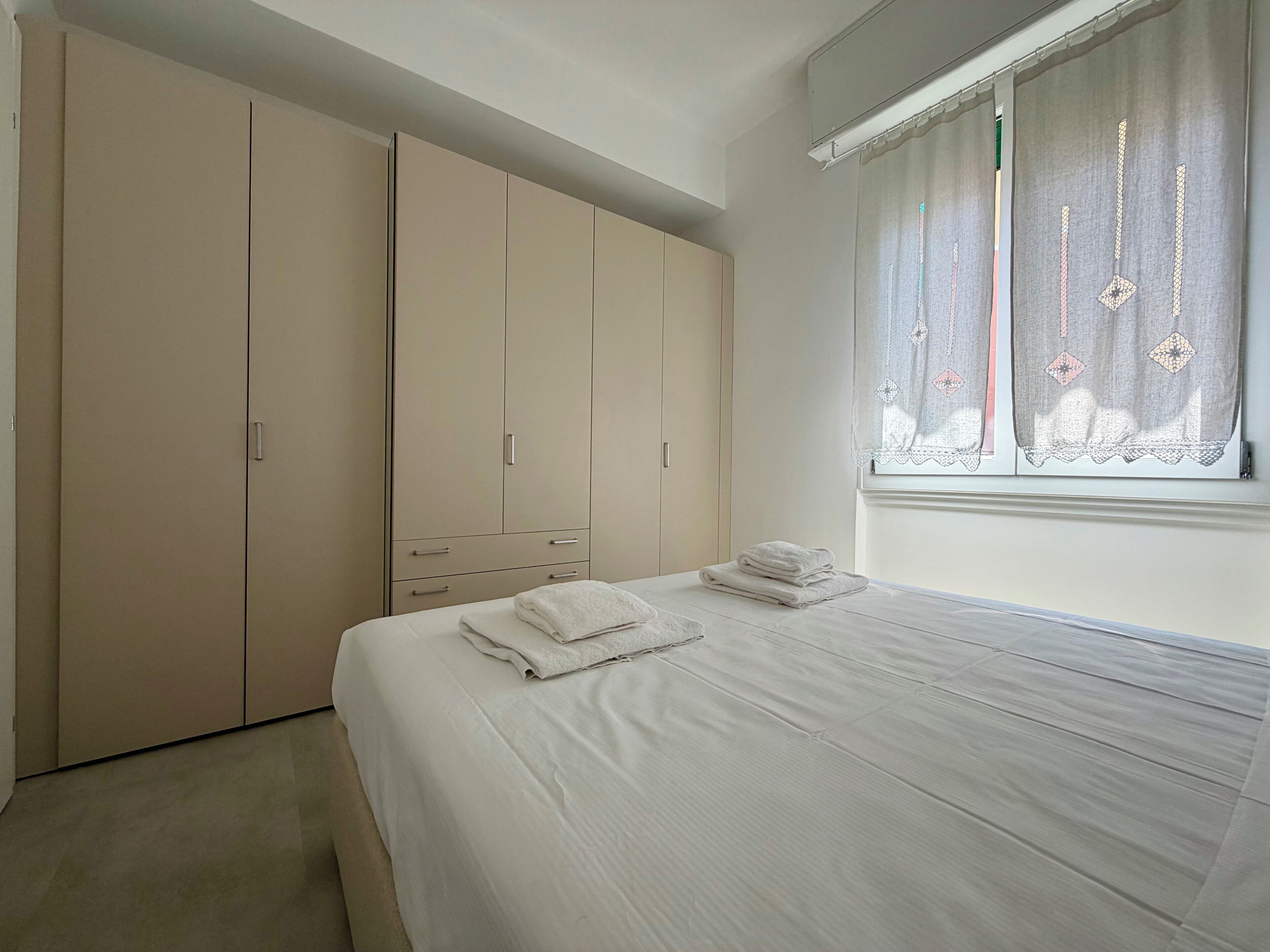 A bedroom with a bed, a wardrobe, and a window with curtains.