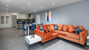 Un saló modern amb un sofà modular, una zona de menjador i una cuina al fons.