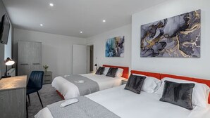 Habitació d'hotel amb dos llits, un escriptori, una cadira i obra d'art a les parets.