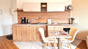 Een compacte keuken met houten kastjes, een koffiezetapparaat, een spoelbak en een eethoek met twee stoelen.