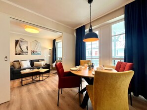 A modern living room with a sofa, dining table, chairs, and artwork on the walls. - Moderne Ferienwohnung mit Balkon in Sellin (Sellin)