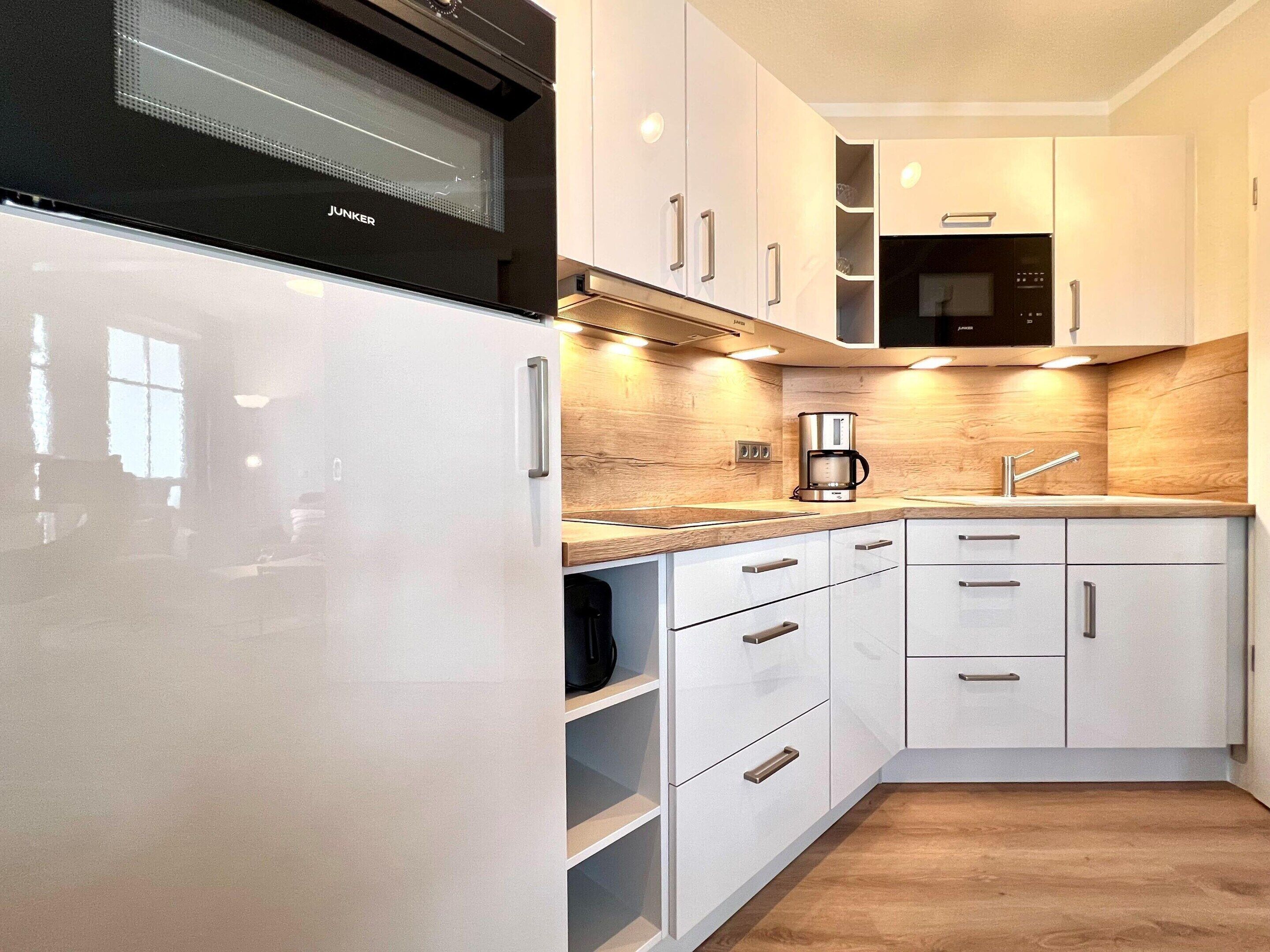 Une cuisine moderne avec des meubles blancs, un micro-ondes noir, une machine à café et un évier en acier inoxydable.
