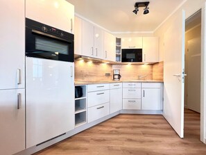 A modern kitchen with white cabinetry, a built-in oven, a microwave, and a coffee maker. - Moderne Ferienwohnung mit Balkon in Sellin (Sellin)