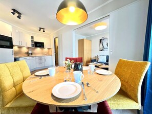A modern dining area with a round wooden table, yellow upholstered chairs, and a central light fixture. - Moderne Ferienwohnung mit Balkon in Sellin (Sellin)