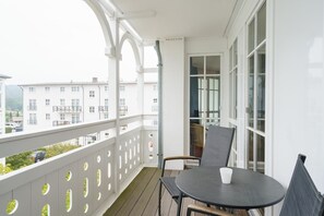 A balcony with a table and chairs, a view of buildings, and a white railing. - Moderne Ferienwohnung mit Balkon in Sellin (Sellin)
