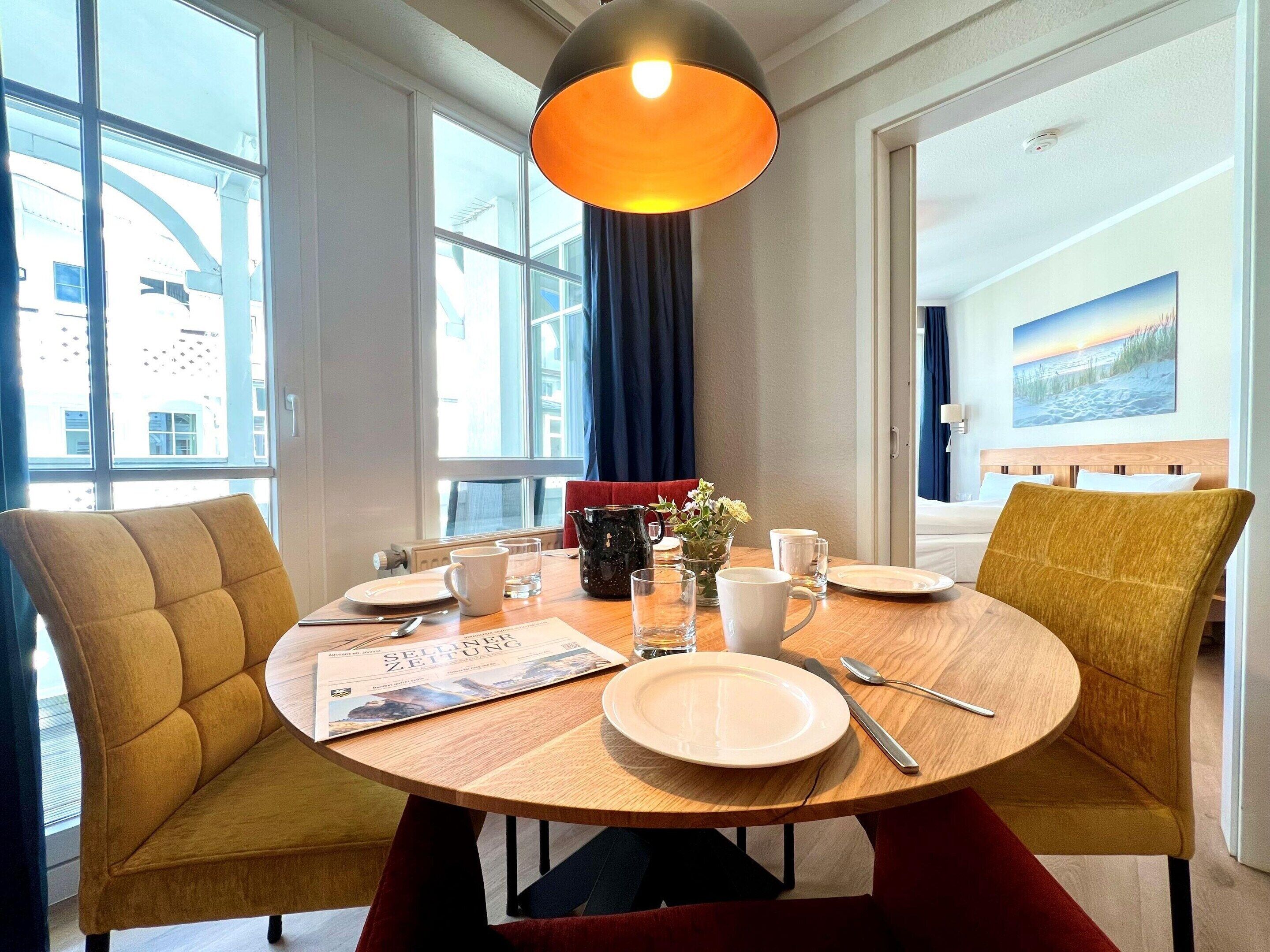 A dining area with a round table, chairs, a magazine, and a vase with flowers.