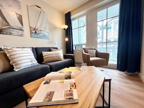 A modern living room with a sofa, armchair, and a coffee table with a magazine. - Moderne Ferienwohnung mit Balkon in Sellin (Sellin)