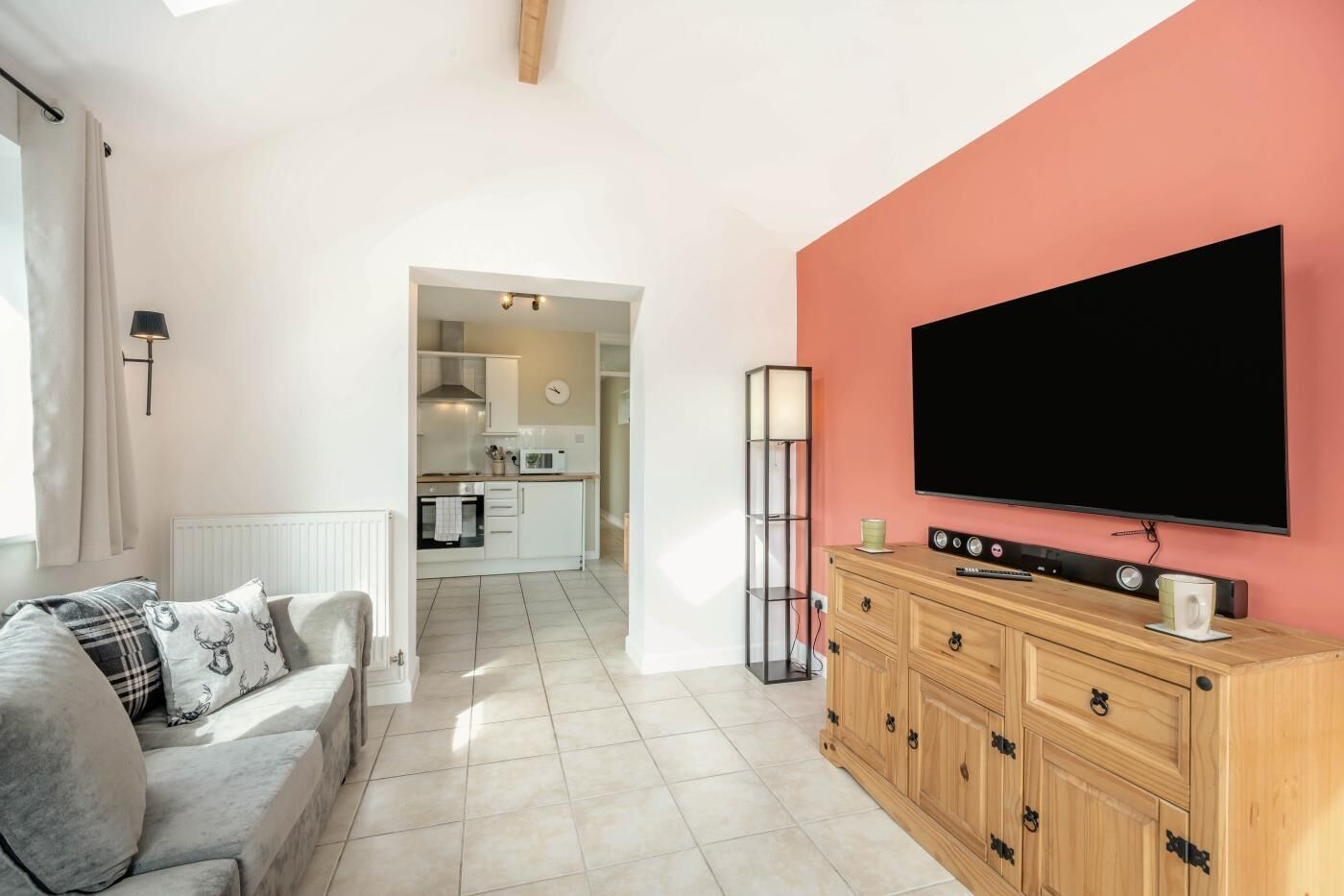 A living room with a sofa, a TV, a wooden cabinet, and a kitchen in the background.
