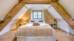 Um quarto com teto inclinado, paredes de pedra, cama com manta fofa, janela com persianas e radiador.