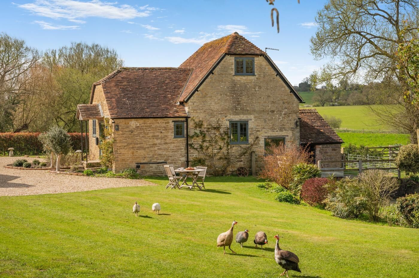 A stone house with a sloped roof, a lawn, and a few turkeys.