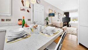 Une cuisine moderne avec un plan de travail en marbre, un coin repas avec une table dressée pour deux personnes et un salon avec un canapé et un téléviseur.