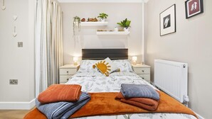 Une chambre à coucher comprenant un lit, des tables de chevet, un radiateur et des étagères murales ornées de plantes et d’objets décoratifs.