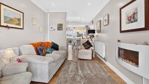 Un salon moderne comprenant un canapé, un fauteuil et une cheminée, et donnant sur une cuisine et un coin repas.