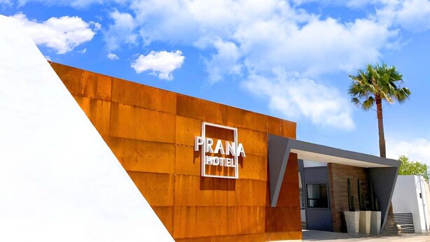 Un edificio moderno con un letrero que dice 'PRANA HOTEL' y una palmera cercana.
