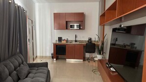 Una cocina moderna con armarios de madera, microondas integrado y una zona de comedor con una silla y una planta.