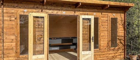 A wooden cabin with a sliding door entrance, a built-in bench, and a small garden area.