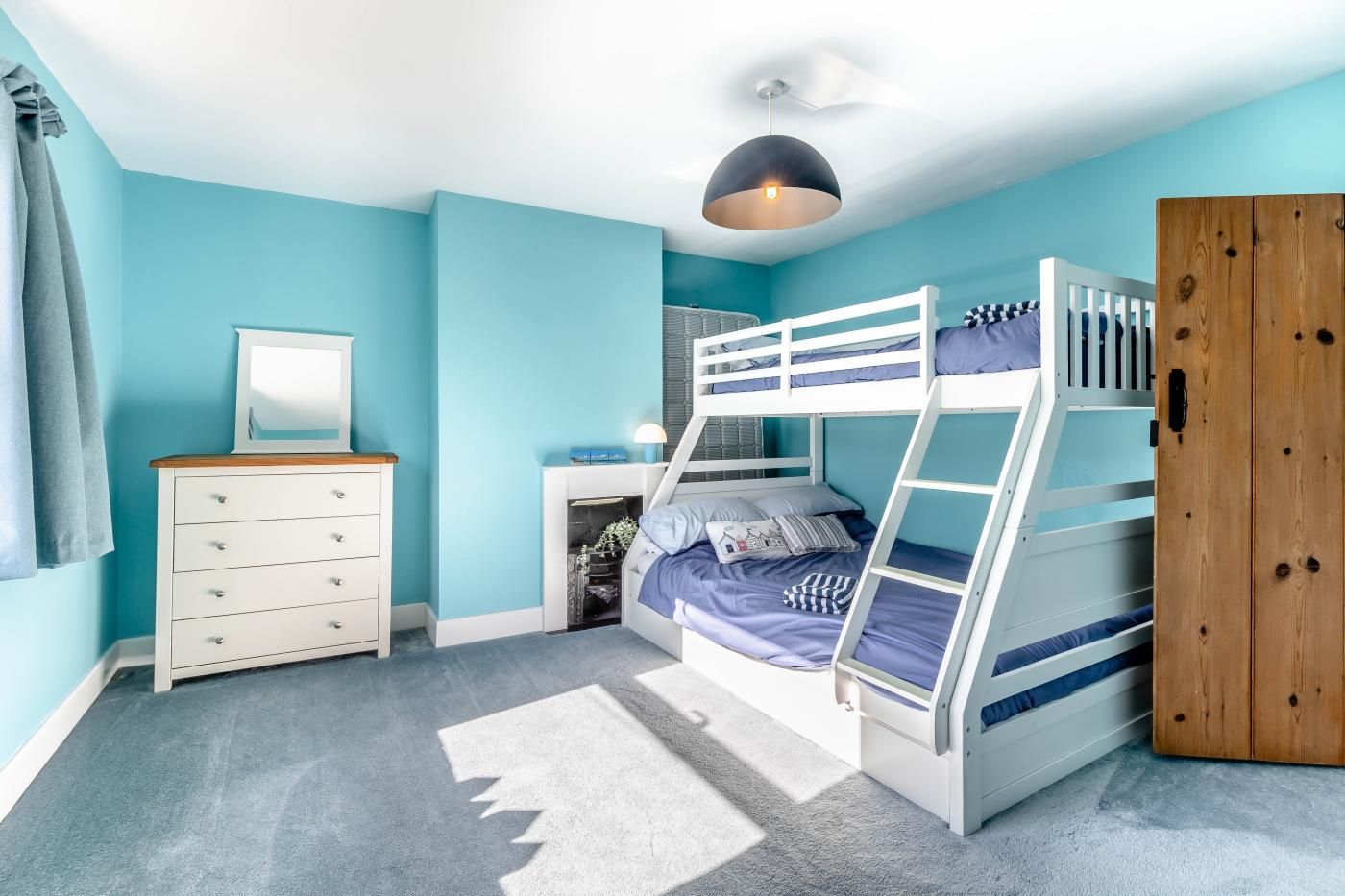 A bunk bed room with a dresser, a mirror, and a wardrobe.