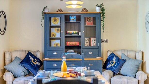 Un coin repas avec une table dressée pour deux personnes, un buffet bleu orné d’objets décoratifs et une horloge au mur.