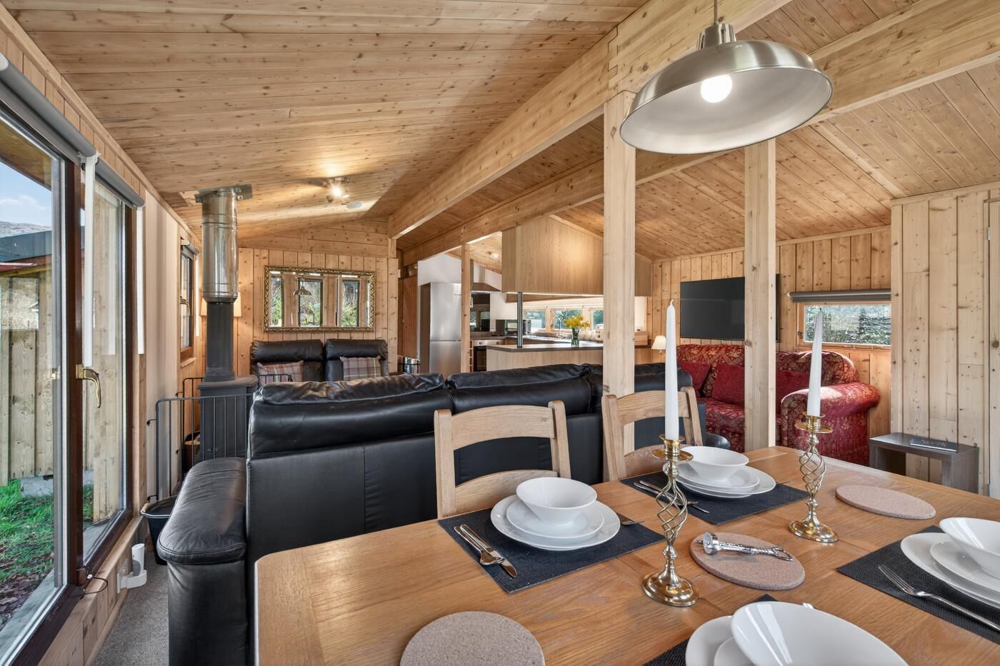 A cozy cabin interior with a dining area, a living room with a sofa, and a kitchen in the background.