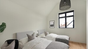 Ett sovrum med två sängar, ett sängbord, en lampa, en hängande taklampa, ett fönster och en växt.