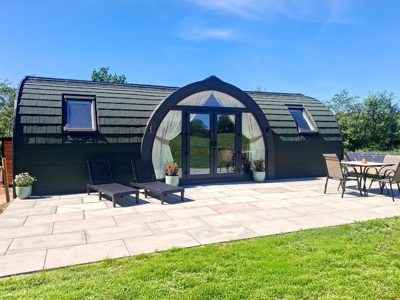 Une maison moderne avec un toit incurvé, un patio doté de mobilier d’extérieur et une grande porte-fenêtre coulissante.