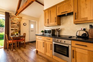 A kitchen with wooden cabinets, a dining table with chairs, and a brick fireplace. - 1 Bed in Gransmoor (oc-s37885) (Gransmoor)