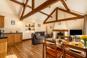A cozy loft-style living space with exposed wooden beams, a kitchen area, a dining table with orange cushions, and a fireplace. - 2 Bed in Gransmoor (oc-c37883) (Gransmoor)