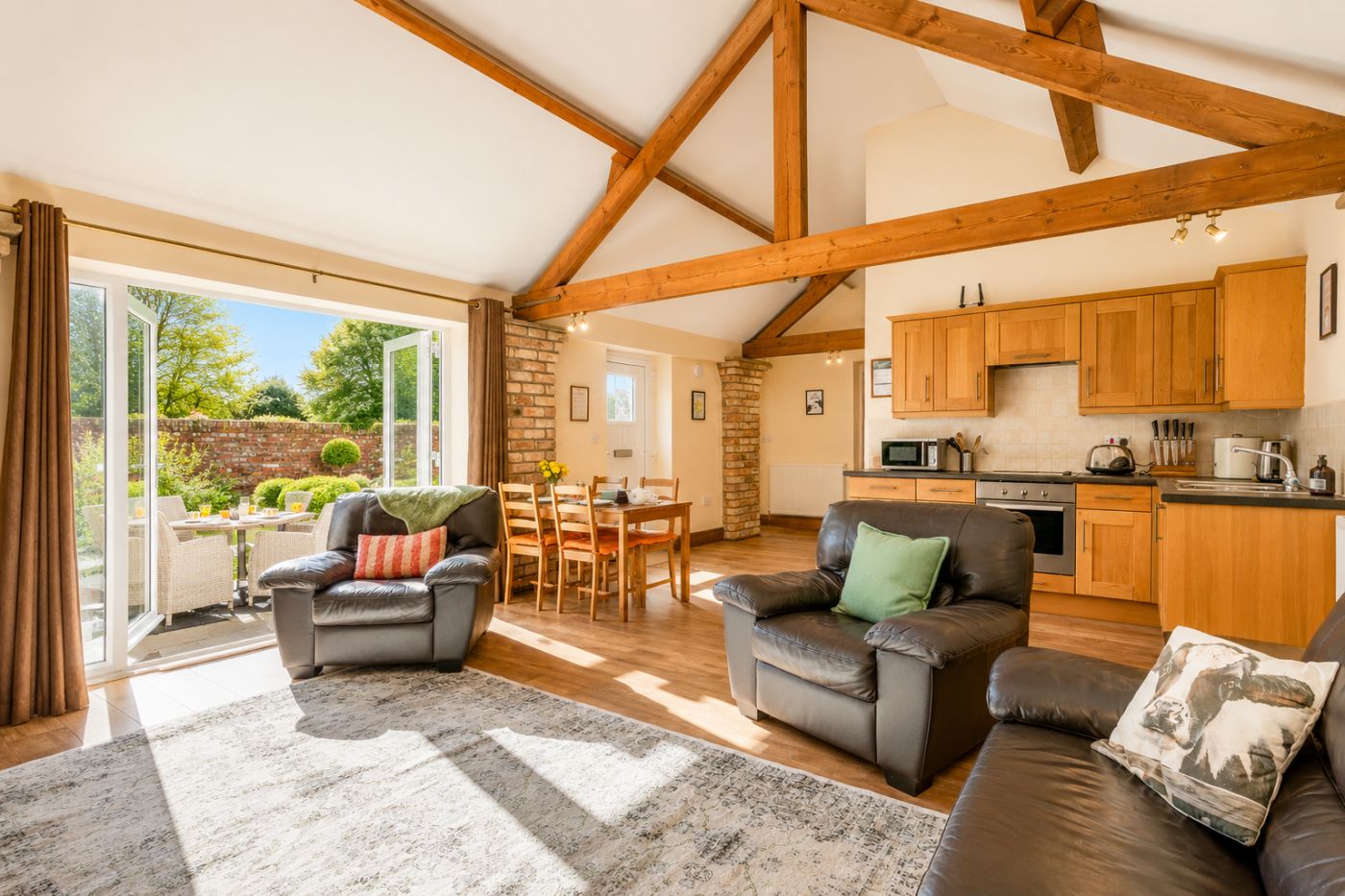 A spacious living area with a dining table, two leather sofas, and a kitchen with wooden cabinets.
