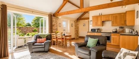 A spacious living area with a dining table, two leather sofas, and a kitchen with wooden cabinets.