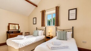 Une chambre d’hôtel avec deux lits, une commode en bois, une table de chevet avec une lampe, une fenêtre avec des rideaux et, au mur, un cadre contenant une citation inspirante.