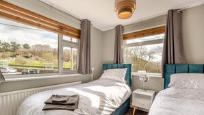A bedroom with two beds, a bedside table with a lamp, and a view of the outside. - 3 Bed in Matlock Moor (oc-m36349) (Matlock)