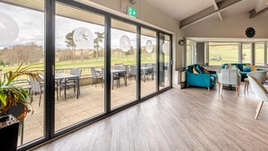 A modern interior with large windows, a dining area, and a seating area with a view of a golf course. - 3 Bed in Matlock Moor (oc-m36349) (Matlock)