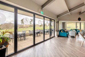 A modern interior with large windows, a dining area, and a seating area with a view of a golf course. - 3 Bed in Matlock Moor (oc-m36349) (Matlock)