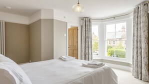 Une chambre à coucher avec un grand lit, une fenêtre avec des rideaux, une porte en bois et un luminaire suspendu.