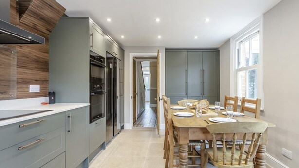 Une cuisine moderne avec des meubles gris, un pare-feu en bois et un coin repas avec une table dressée pour quatre personnes.