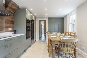 A modern kitchen with grey cabinets, a wooden backsplash, and a dining area with a table set for four. - 3 Bed in Southwold (oc-n37503) (Southwold)